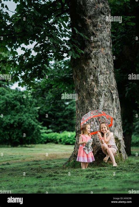 Zwei Junge Blonde M Dchen Versteckt Unter Einem Bunten Schirm Unter Einem Baum Stockfotografie