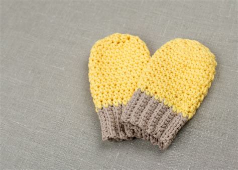 Two Yellow And Gray Mittens Sitting On Top Of A Grey Cloth Covered