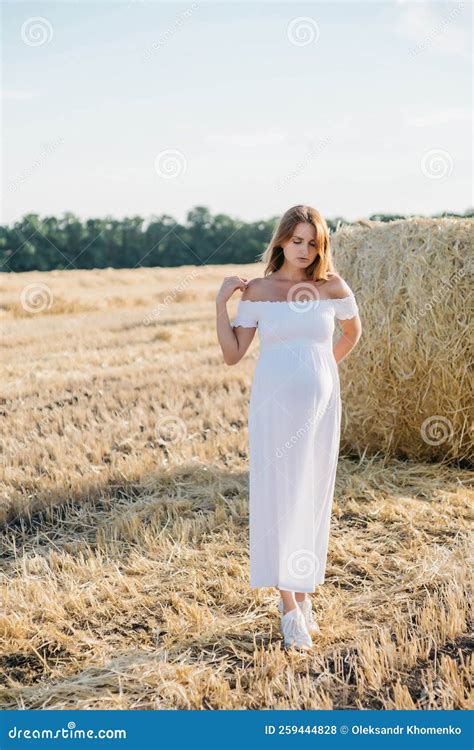 Beautiful Pregnant Brunette In A White Dress Near The Haystacks In The