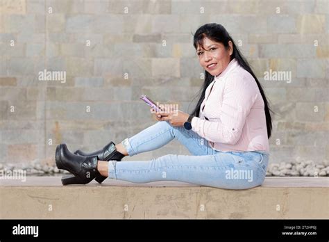 Mature Latina Woman Interacting With Her Mobile Striped Shirt On Worn Jeans Stock Photo Alamy