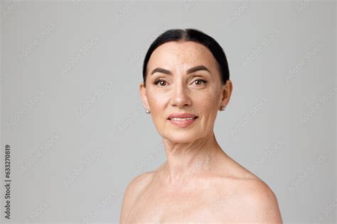 Portrait Of Smiling Beautiful Dark Heared Mature Woman With Bare Shoulders Looking At Camera