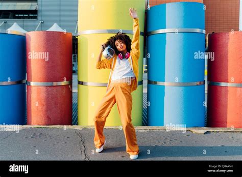 Young Woman Carrying Boom Box On Shoulder Dancing In Front Of Colorful