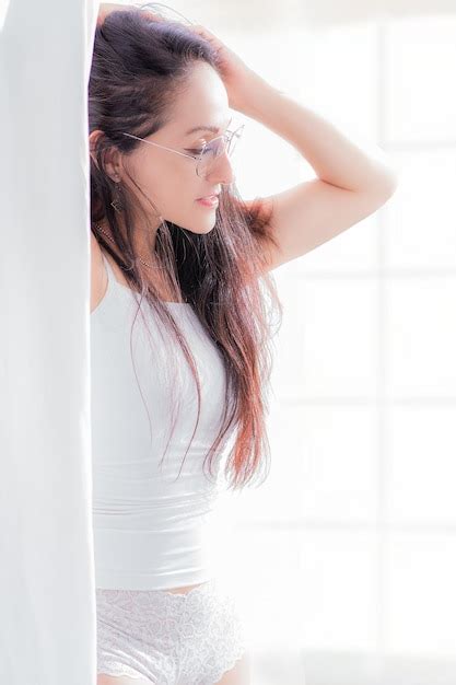 Hermosa mujer latina en lencería blanca de pie junto a una ventana ella es muy feliz posando