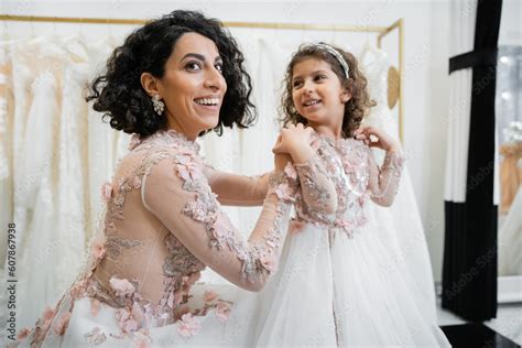 Happy Middle Eastern Woman With Brunette Hair In Floral Wedding Dress Hugging Smiling Daughter