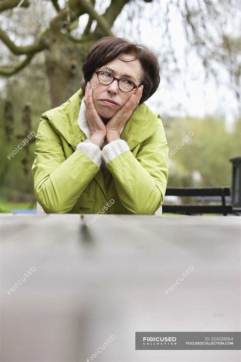 Tired Thoughtful Woman Leaning On Elbows At Table Outdoors