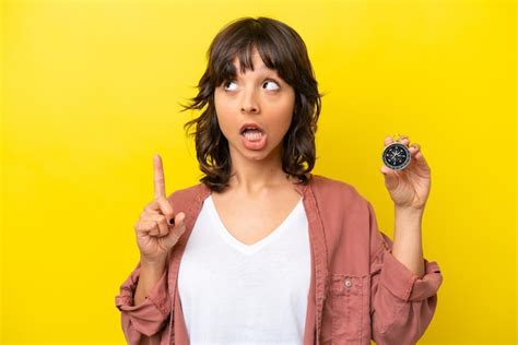 Jovem mulher latina segurando bússola isolada em fundo amarelo pensando em uma ideia apontando o