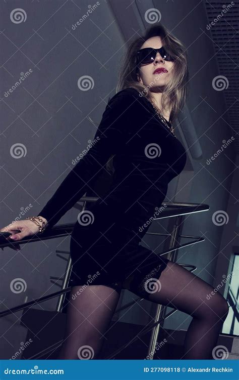 Blonde Total Black In A Short Dress Stockings And Black Stiletto Shoes Strolls Down The Stairs
