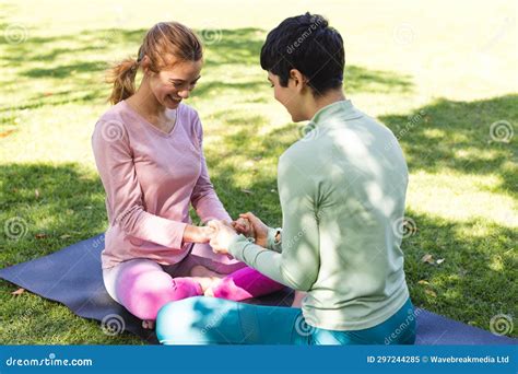 Happy Biracial Lesbian Couple Practicing Yoga Sitting Holding Hands And Smiling In Sunny Garden