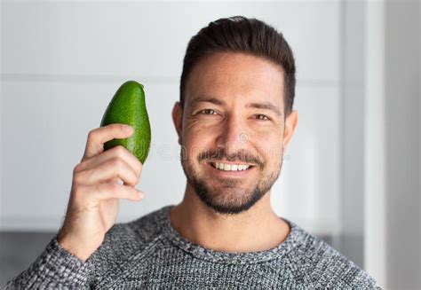 Happy Young Man With Toothy Smile Holding Avocado In Kitchen Stock