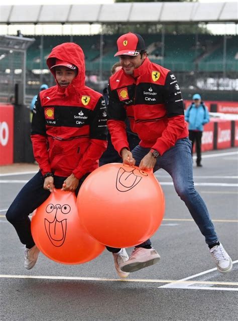 Two Men In Red Jackets Carrying Large Orange Balls On Their Backs And