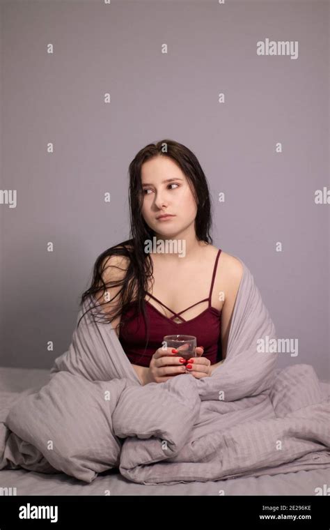 Charming Sleepy Brunette Woman With Glass Cup Of Tea In Bed With Grey Bed Linens Morning