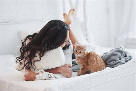 Looking At The Cat Attractive Blonde Resting On The White Bed With Her Cute Kitten Stock Image