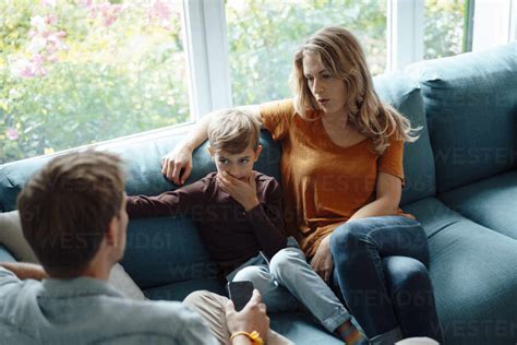 Blonde Frau sitzt neben ihrem Sohn und unterhält sich mit einem Mann auf dem Sofa im Wohnzimmer