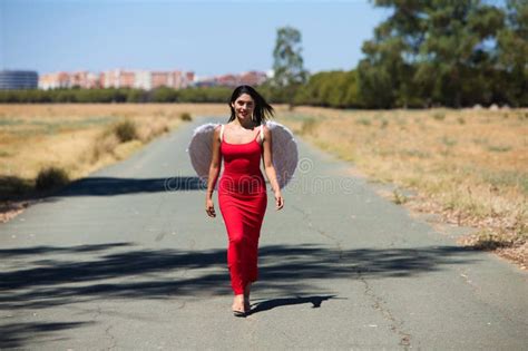 Bella Joven Latina Vestida De Seda Roja Y Alas Blancas Camina A Lo Largo De Un Camino Asfaltado