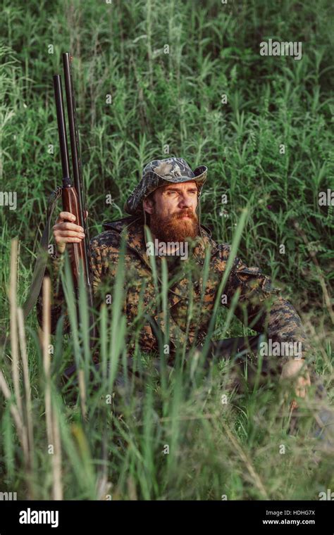 Hunter Holding Rifle While Sitting On Grassy Field Stock Photo Alamy
