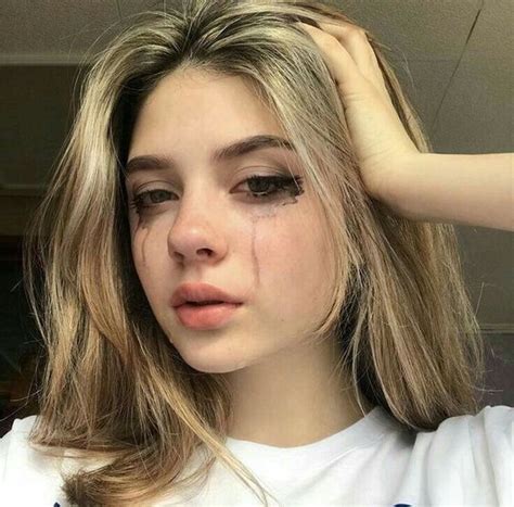 A Woman With Long Blonde Hair And Eyeliners Is Looking At The Camera While Wearing A White T Shirt