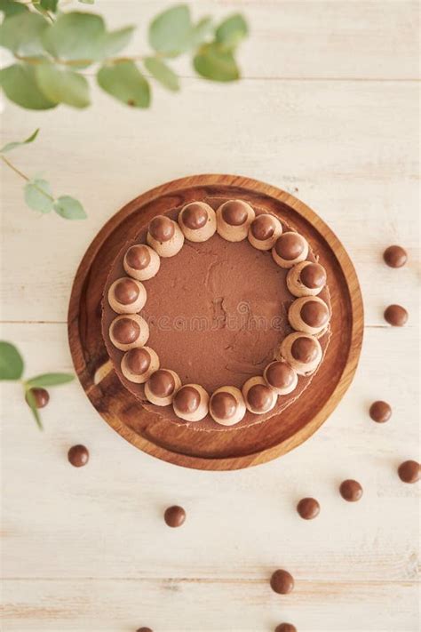 Vertical Shot Of A Delicious Chocolate Naked Cake With Choco Balls And Cream On A White Table