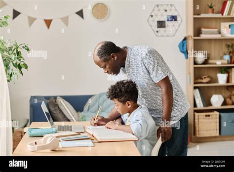African Mature Tutor Helping Schoolboy To Do His Homework While He Sitting At Table With Books