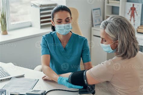 Young female nurse using monitoring equipment to check mature woman ...