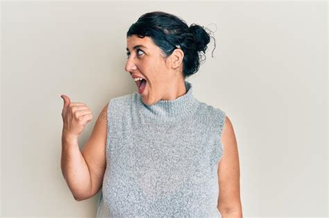 Plus Size Brunette Woman Wearing Casual Clothes Pointing Thumb Up To The Side Smiling Happy With