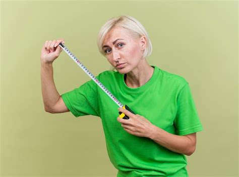 Femme slave blonde d âge moyen à l avant tenant mètre ruban isolé sur mur vert olive Photo