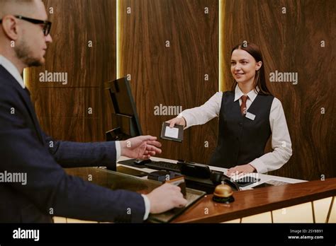 Medium Close Up Of Brunette Receptionist Giving Passport And Room Key To Hotel Guest Stock Photo