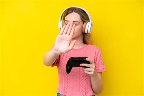 Blonde jeune fille anglaise jouant avec un contrôleur de jeu vidéo isolé sur fond jaune Photo