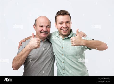 Two Caucasian Mature Men Father And Son Holding Thumbs Up Approving Your Choice Studio Shot