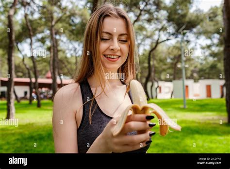 Cute Brunette Woman Wearing Sports Bra Standing On City Park Outdoors Eating Healthy Banana For