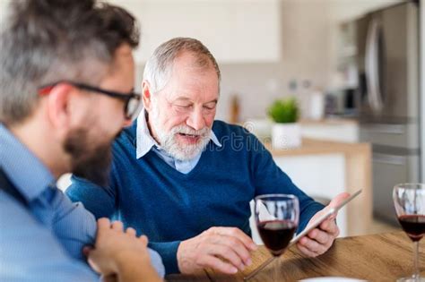 Adult Son And Senior Father Sitting At The Table Indoors At Home Using