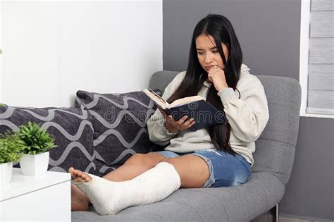 30 Year Old Latina Woman Reads A Book In Her Living Room While Recovering From Her Leg That Was
