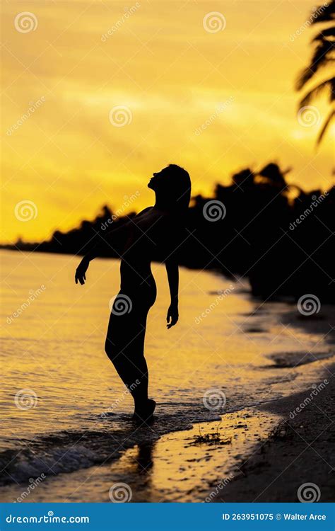 A Nude Latin Model Poses Against The Colorful Sky As The Sun Rises On The Pacific Ocean In Baja