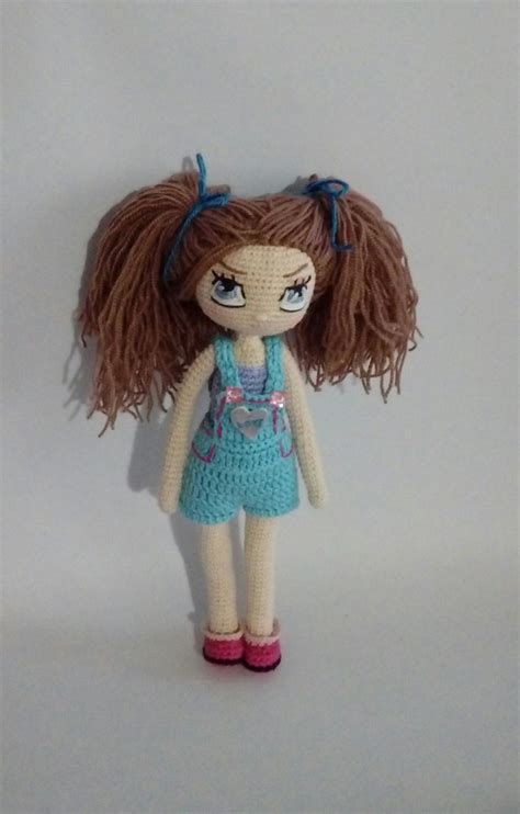 A Crocheted Doll With Brown Hair And Blue Dress Standing On A White Surface