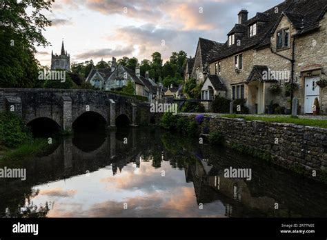 The Sun Sets Over The Quaint Cotswold Stone Cottages And Arch Bridge Of