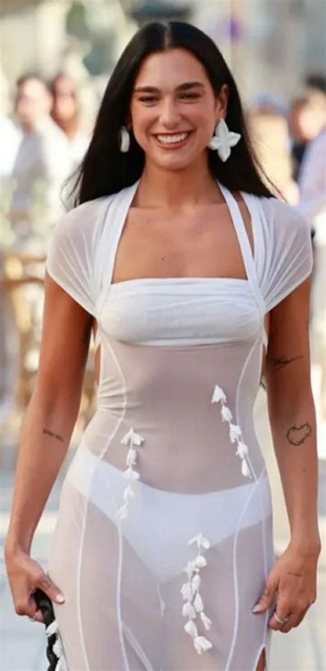 A Woman In A White Bodysuit Walking Down The Street With Her Hand On