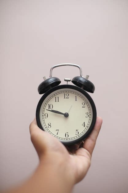 Premium Photo Cropped Hand Holding Alarm Clock Against Gray Background