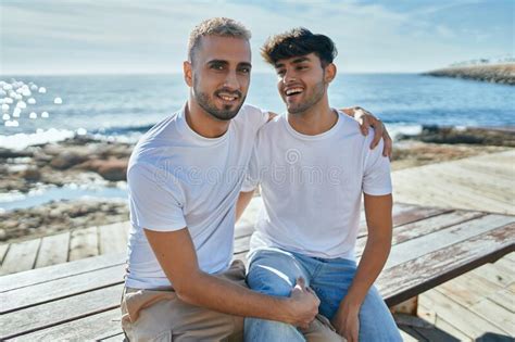 Joven Pareja Gay Sonriendo Feliz Sentado En El Banco En El Paseo De La Playa Imagen De Archivo