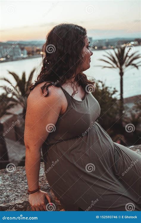 Brunette Curly Chubby Girl Wearing A Brown Dress Looking At The Sea At Sunset Between Palms