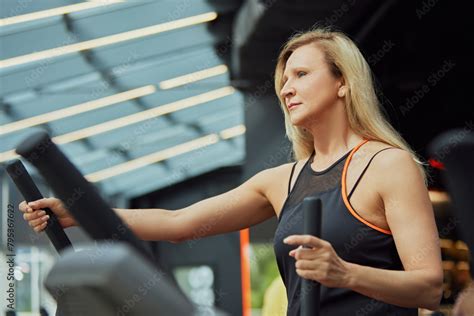 Mature Woman In Workout Gear Using An Elliptical Trainer Focused On