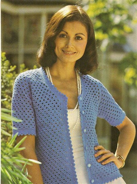 A Woman Wearing A Blue Crocheted Cardigan And White Dress Is Posing For