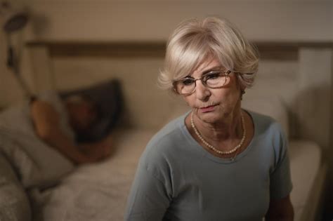 Femme Mature Réfléchie Assise Dans La Chambre Le Soir Pendant Que Son Mari Dort En Arrière plan