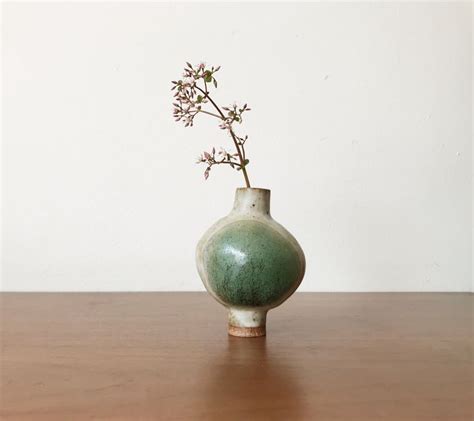 A Green Vase With Some Pink Flowers In It On A Wooden Table Next To A