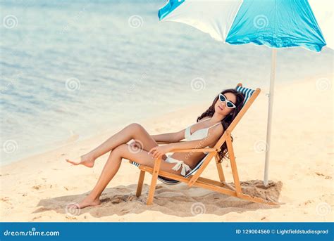 Woman In Sunglasses And Bikini Relaxing On Beach Chair Under Umbrella