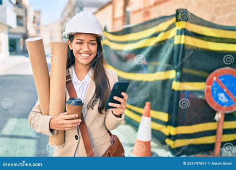 Joven Arquitecta Latina Sostiene Planos Y Usa Smartphone En La Ciudad Imagen De Archivo Imagen