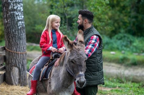 Premium Photo On A Farm A Cute Blonde Girl Riding A Donkey On A Farm Her Dad Helping Her