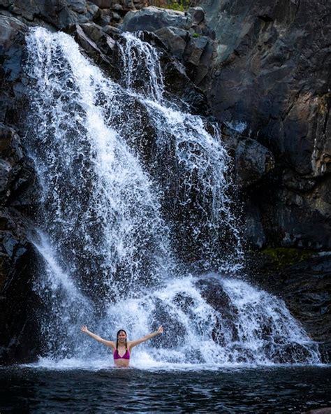 Una Hermosa Chica En Bikini Rosa Se Encuentra Debajo De Una Cascada En Una Piscina Natural