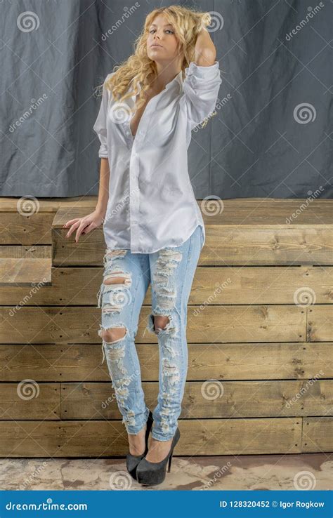 Blonde Hermoso Joven De La Muchacha En Una Camisa Blanca Y Vaqueros Con Huecos Foto De Archivo