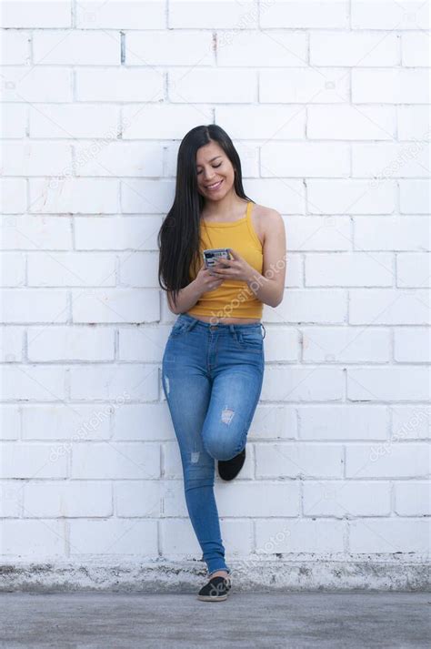 hermosa mujer latina escribiendo en su teléfono celular apoyada en una pared blanca