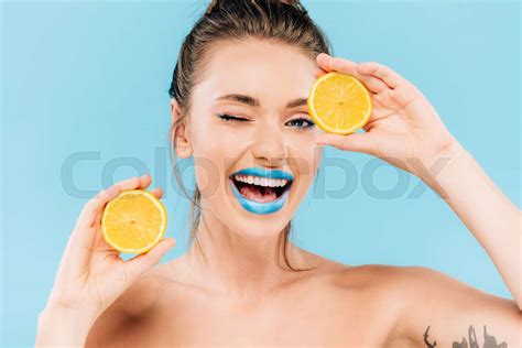 Happy Winking Naked Beautiful Woman With Blue Lips Holding Orange Halves Isolated On Blue