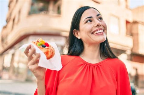 Joven Latina Sonriendo Feliz Comiendo Dulces Caminando Por La Ciudad Foto Premium